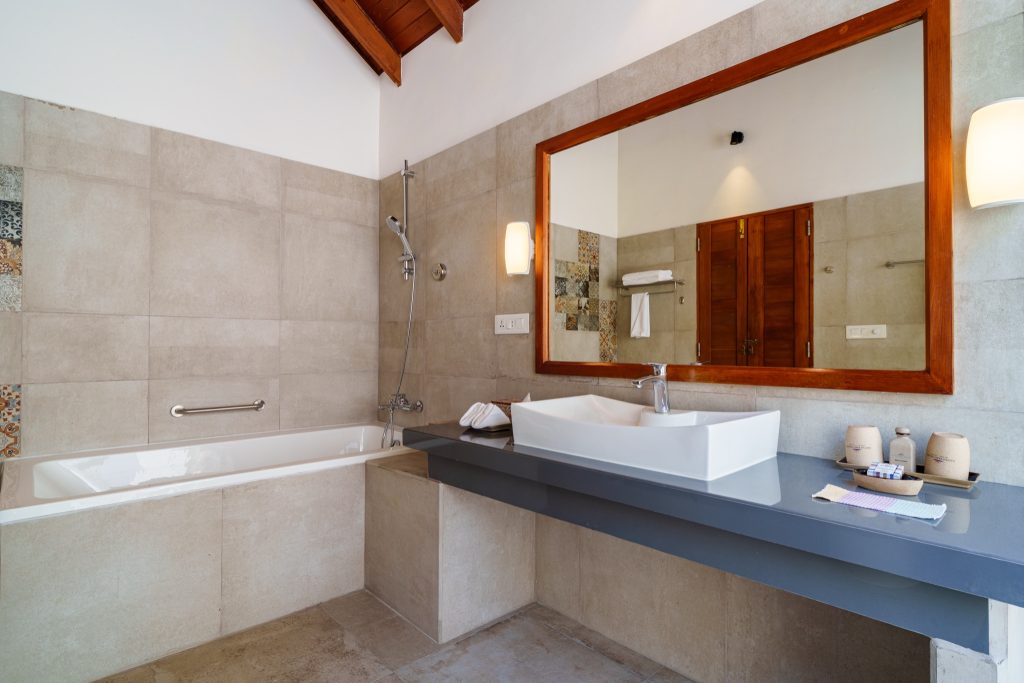 Badezimmer der Deluxe Beach Villa im Reethi Faru Resort mit weißer Badewanne, Duscharmatur, Spiegel