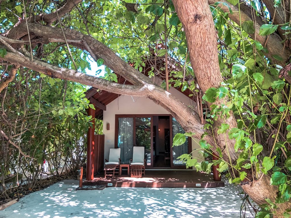 Eingang der Deluxe Beach Villa im Reethi Faru Resort mit Holzterrasse, zwei Holzliegen mit weißen Polstern