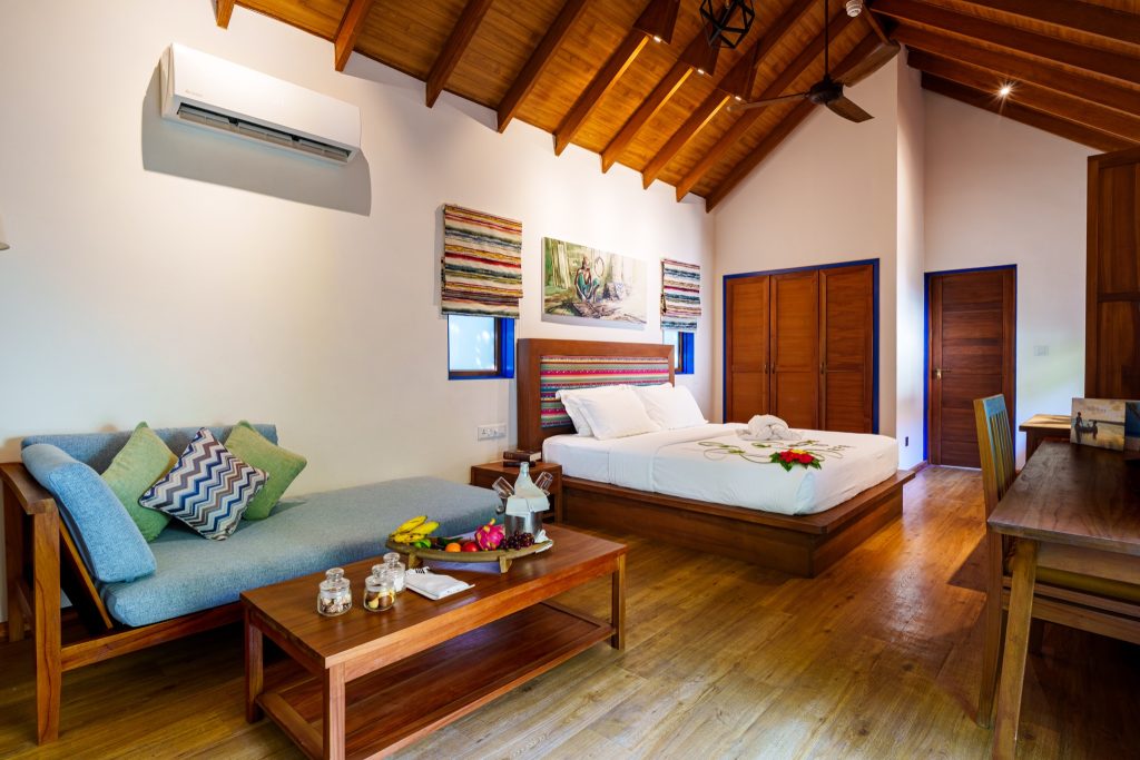 Helles Zimmer der Garden Villa im Reethi Faru Resort mit Holzboden, großem Bett, Sofa und bunten Kissen