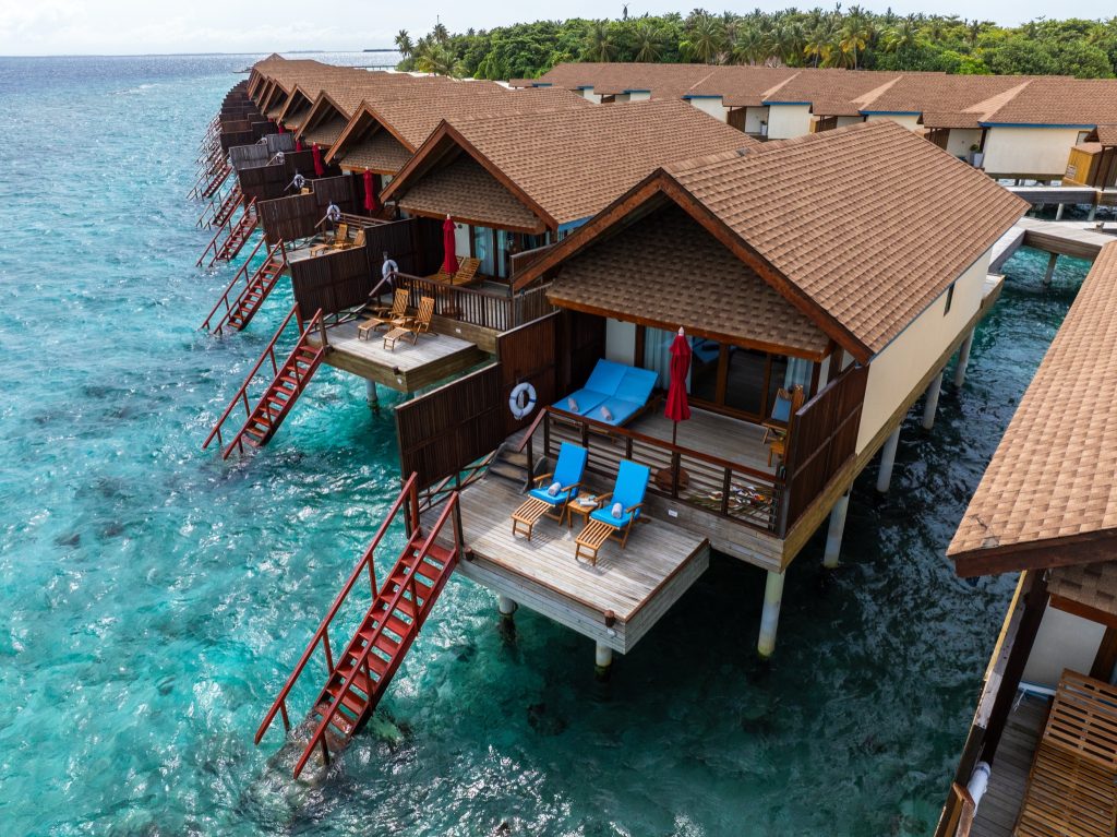 Reihe von Wasserbungalows mit Holzdächern und Veranden über türkisblauem Meer im Reethi Faru Resort