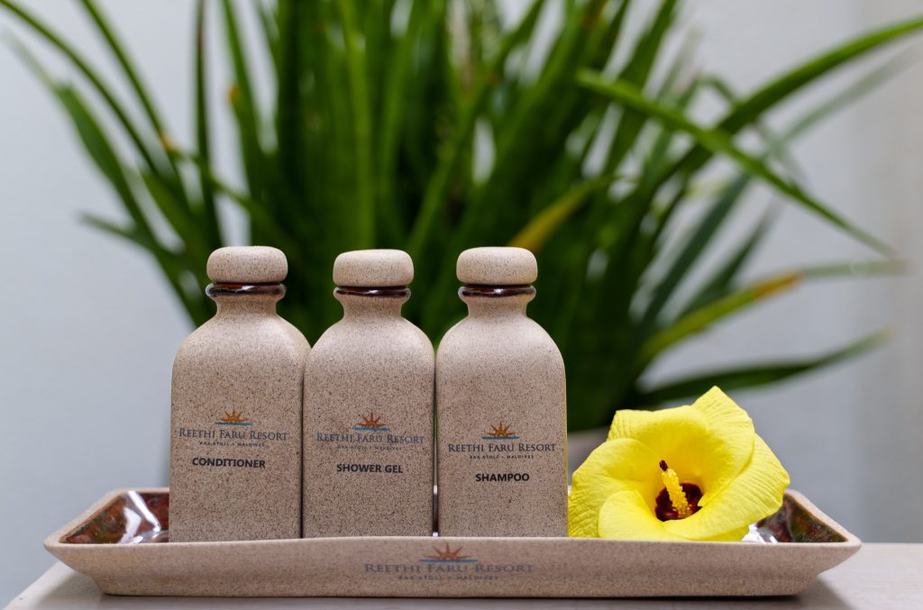 Drei gleichförmige Flaschen mit Conditioner, Shower Gel und Shampoo auf rechteckigem Tablett mit gelber Blume