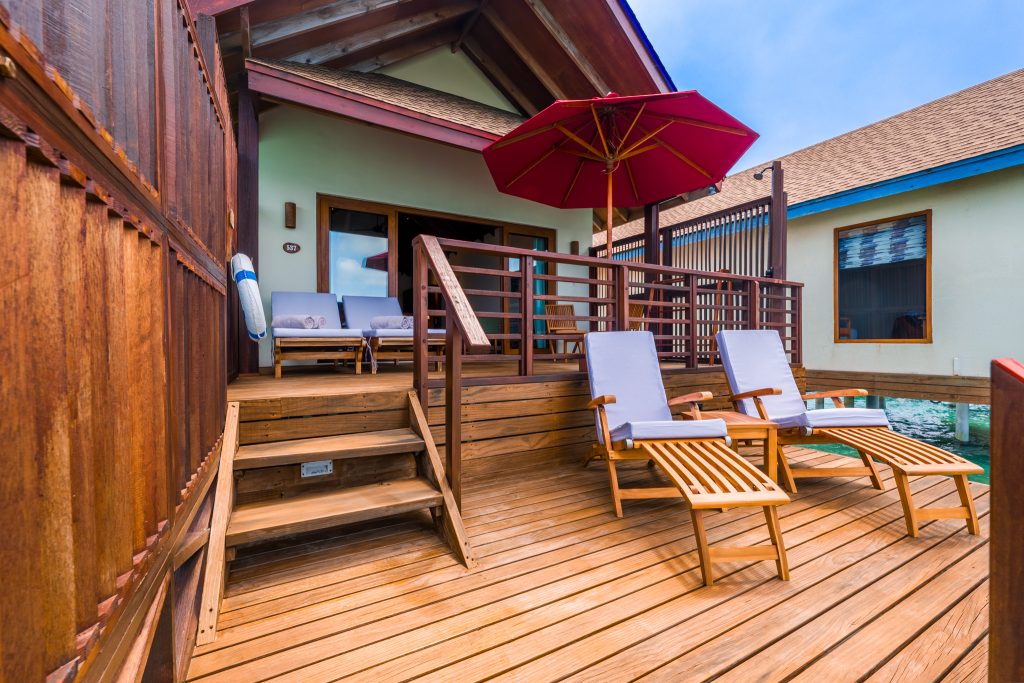 Hölzerne Terrasse einer Water Villa im Reethi Faru Resort mit zwei Deckstühlen unter rotem Sonnenschirm