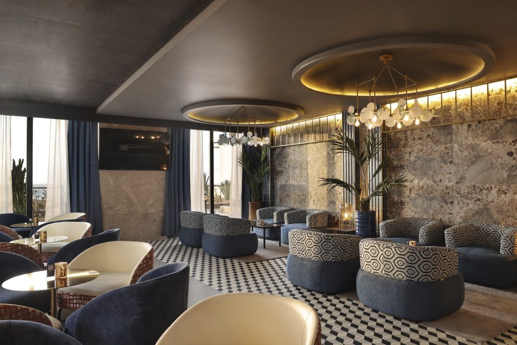 Bar Elite Club Lounge mit blauen und beigen Sesseln, schwarz-weißem Bodenmuster und großen Fenstern im Hotel Riu Palace.