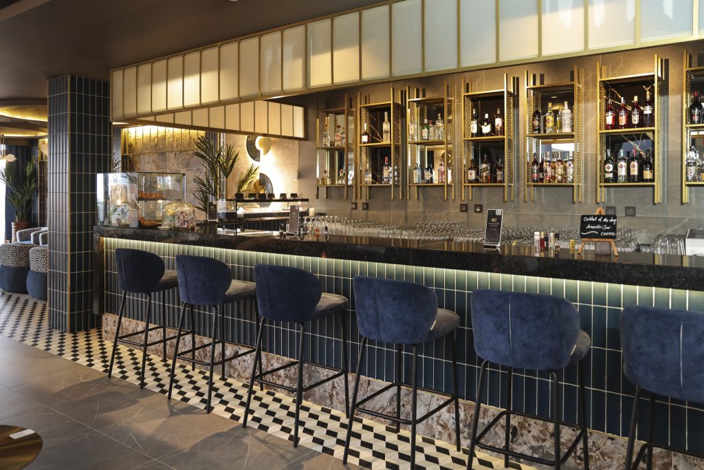 Barbereich mit schwarzer Stein-Theke, dunkelblauen Samt-Barhockern und goldfarbenen Glasregalen im Hotel Riu Palace Swahili