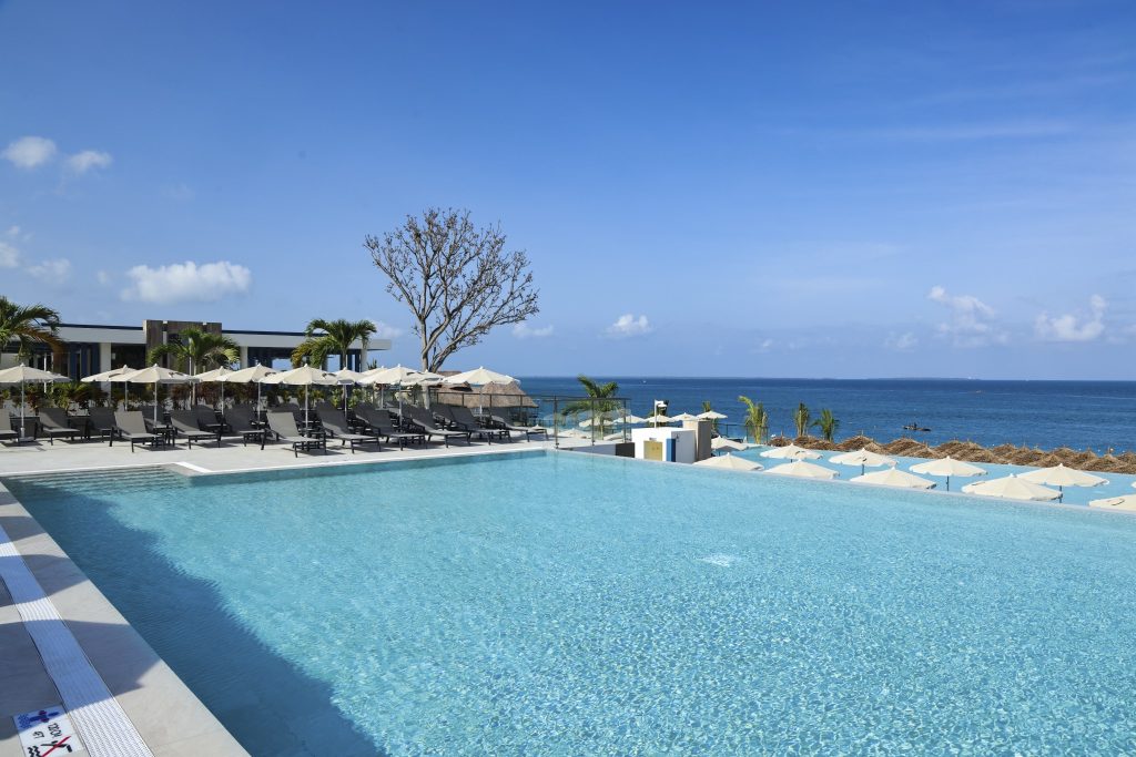 Großer rechteckiger Pool mit grauen Sonnenliegen und beigefarbenen Sonnenschirmen im Außenbereich des Hotels Riu Palace.