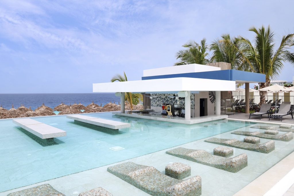 Moderner Hotelpool mit Poolbar, geflieste Liegen im flachen Wasser und Palmen im Hintergrund in Sansibar