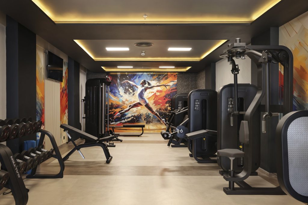 Fitnessraum im Hotel Riu Palace Swahili mit Hanteln, Kraftgeräten und farbigem Wandbild in Grau und Schwarz