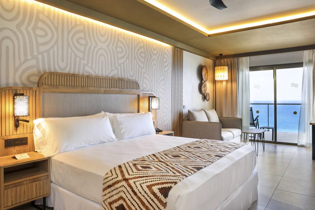 Junior Suite Sea View mit Holzbett, beigem Sofa und Glas-Schiebetür zum Balkon mit Meerblick im Hotel Riu Palace Swahili
