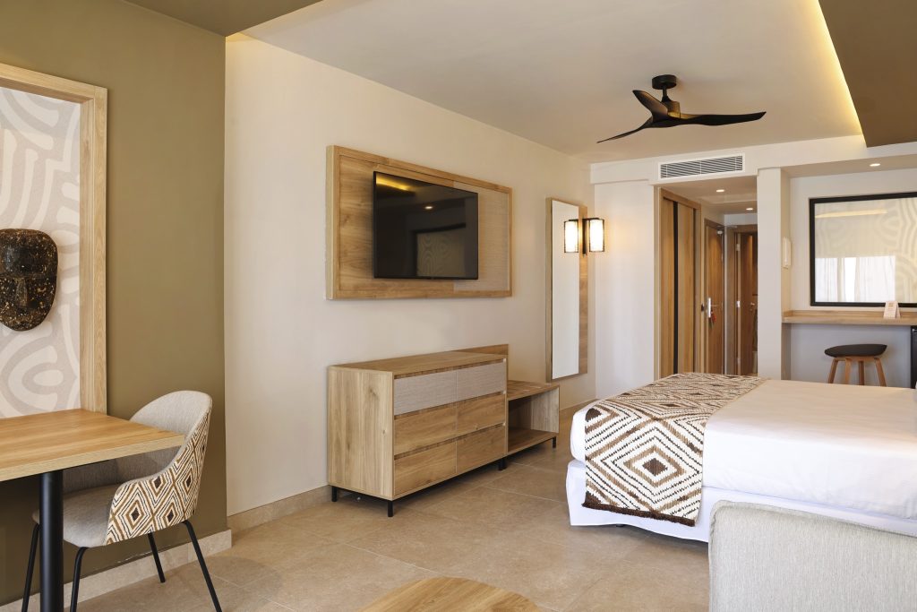 Modernes Hotelzimmer Junior Suite Sea View mit Holzkommode, Tisch, Bett und Fernseher an der Wand im Hotel Riu Palace Swahili