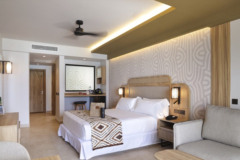 Modernes Hotelzimmer mit großem Bett, weißer Bettwäsche und Erdtönen, geometrischer Wandtapete und Holzmöbeln