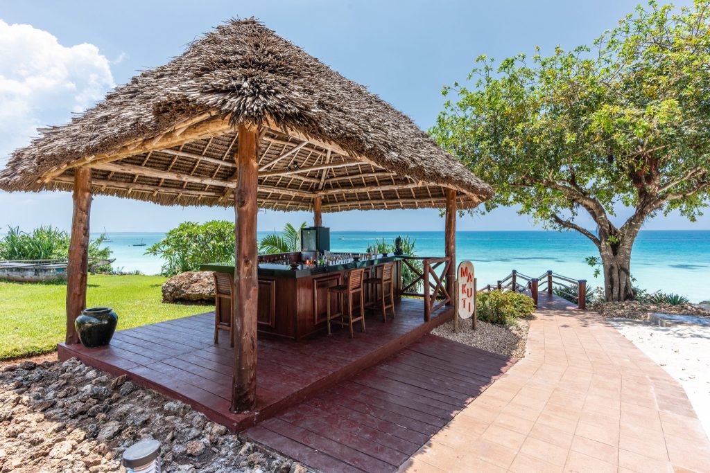 Offene Strandbar mit strohgedecktem Dach, Holzmöbeln und Blick auf das türkisfarbene Meer in Sansibar