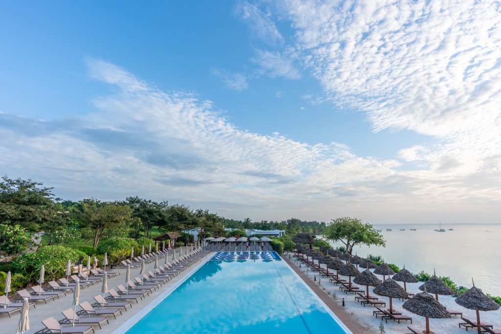 Rechteckiger Außenpool am Riu Palace Zanzibar mit zwei Reihen Liegestühlen und strohfarbenen Sonnenschirmen
