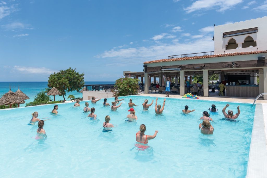 Mehrere Personen nehmen an einer Wassergymnastik im klaren blauen Pool des Riu Palace Zanzibar teil.