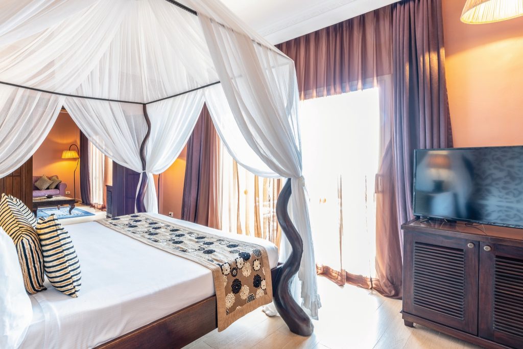 Hotelzimmer der Beach Villa im Riu Palace Zanzibar mit Himmelbett, weißen Vorhängen und lilafarbenem Sofa
