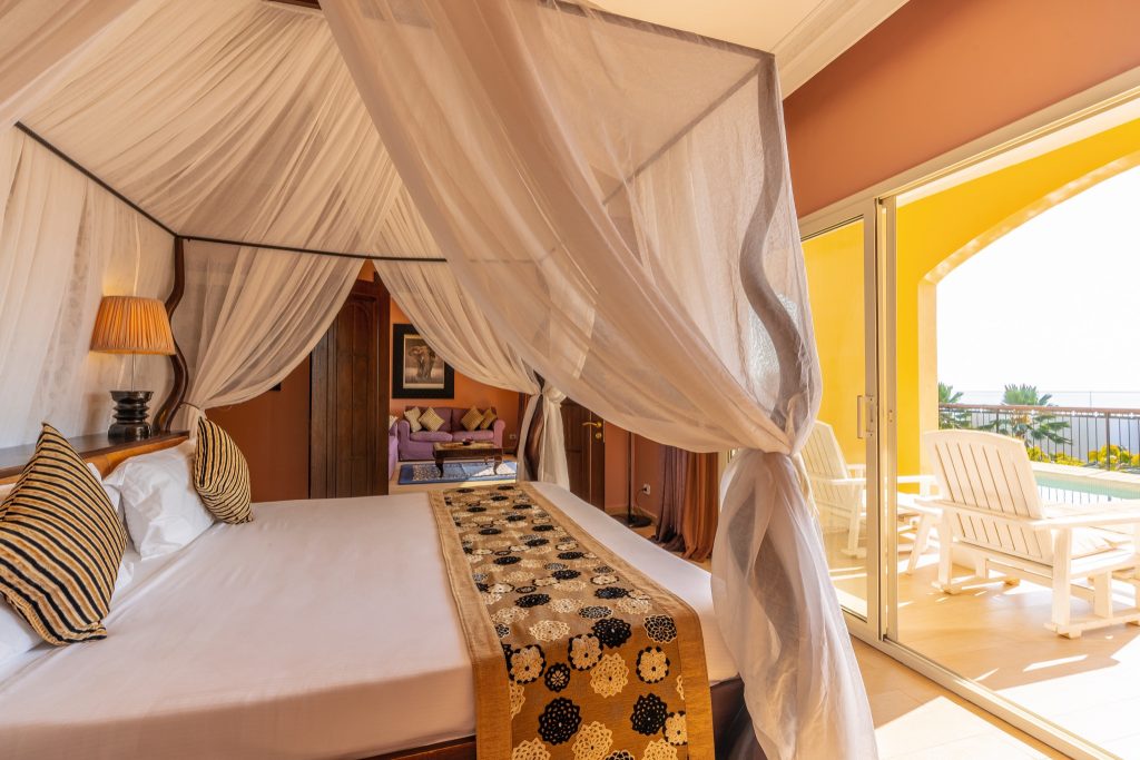 Zimmer Beach Villa im Riu Palace Zanzibar mit Himmelbett, Terrakotta-Wänden, Balkon und zwei weißen Liegestühlen