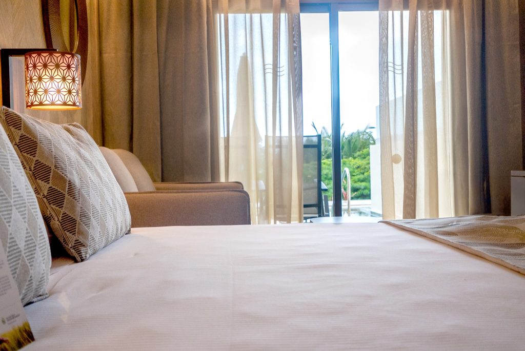 Modernes Zimmer der Junior Suite Swim Up im Riu Palace Zanzibar mit Bett, Lampe und Terrasse mit Poolblick