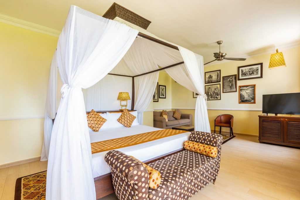 Hotelzimmer im Riu Palace Zanzibar mit Himmelbett, weißen Vorhängen, Sofa, Fernseher und warmem Tageslicht