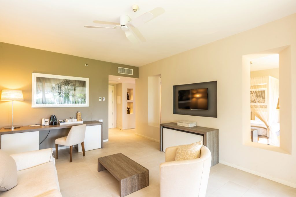 Zimmer Superior Ocean Suite mit beigem Sofa, Holztisch, Schreibtisch, Flachbildfernseher und Himmelbett in angrenzendem Raum
