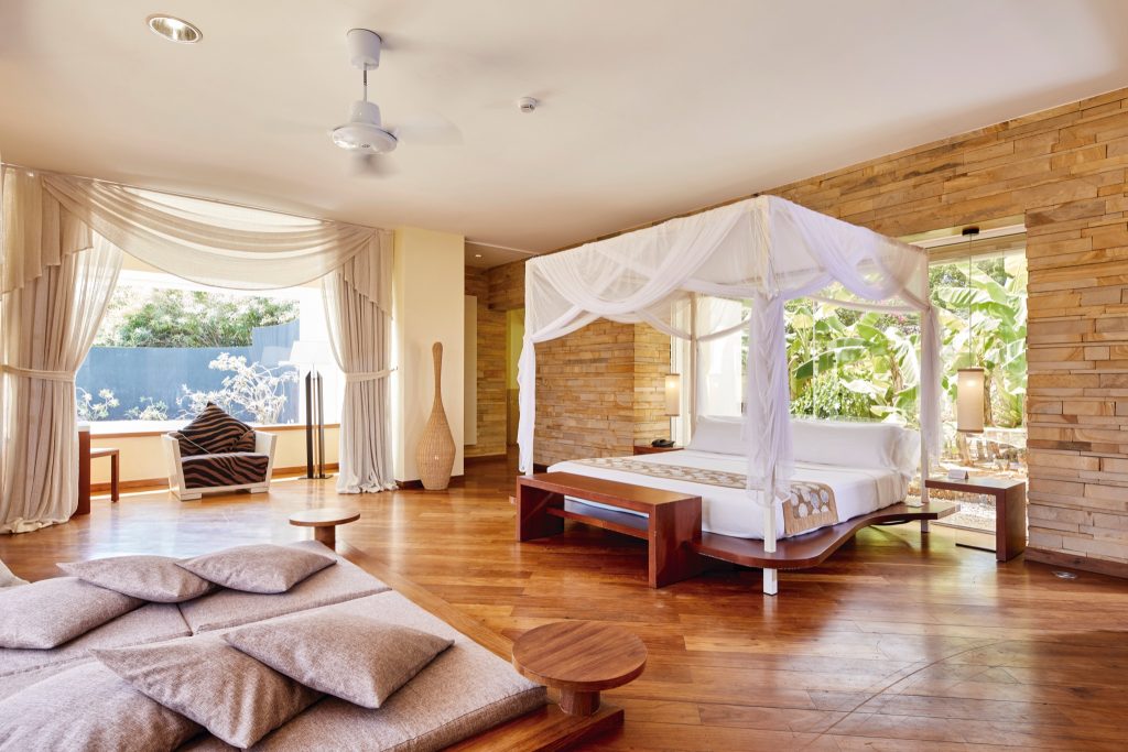 Helles Hotelzimmer im Riu Palace Zanzibar mit weißem Baldachinbett, Holzfußboden und großen Fenstern