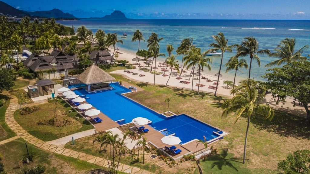 Großer rechteckiger Pool mit weißen Sonnenschirmen, blauen Liegen und Palmen am Sandstrand auf Mauritius