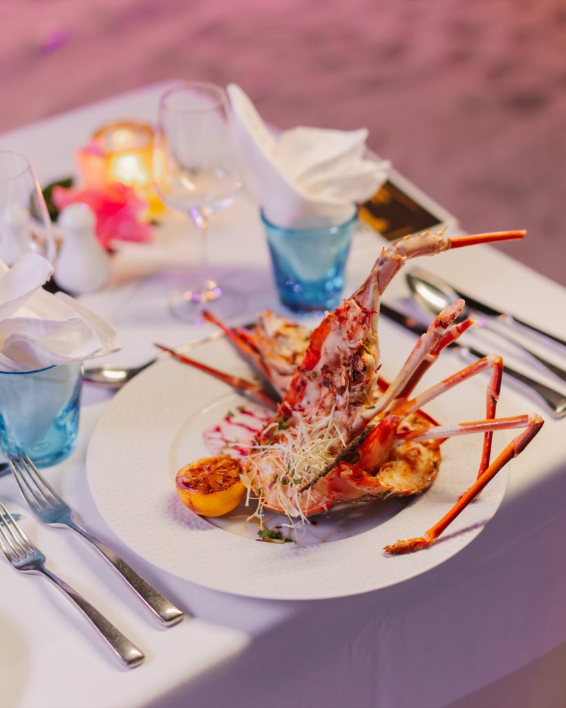 Tisch im restaurant-lobster-01 mit Hummer, gegrillter Zitrone, Sprossensalat, weißem Stoff und Metallbesteck