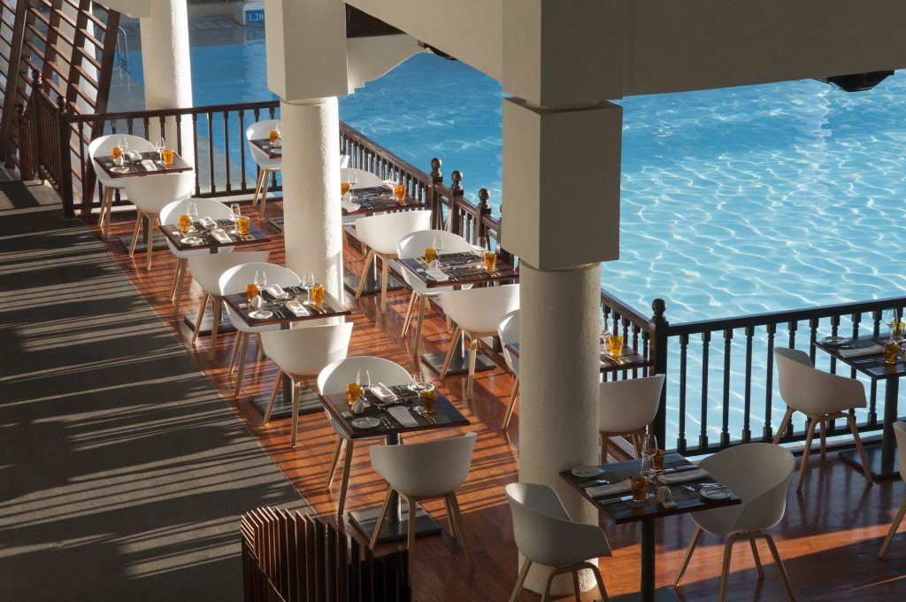 Überdachte Terrasse des Restaurants Ravinala mit weißen Tischen, Stühlen und Blick auf blauen Pool