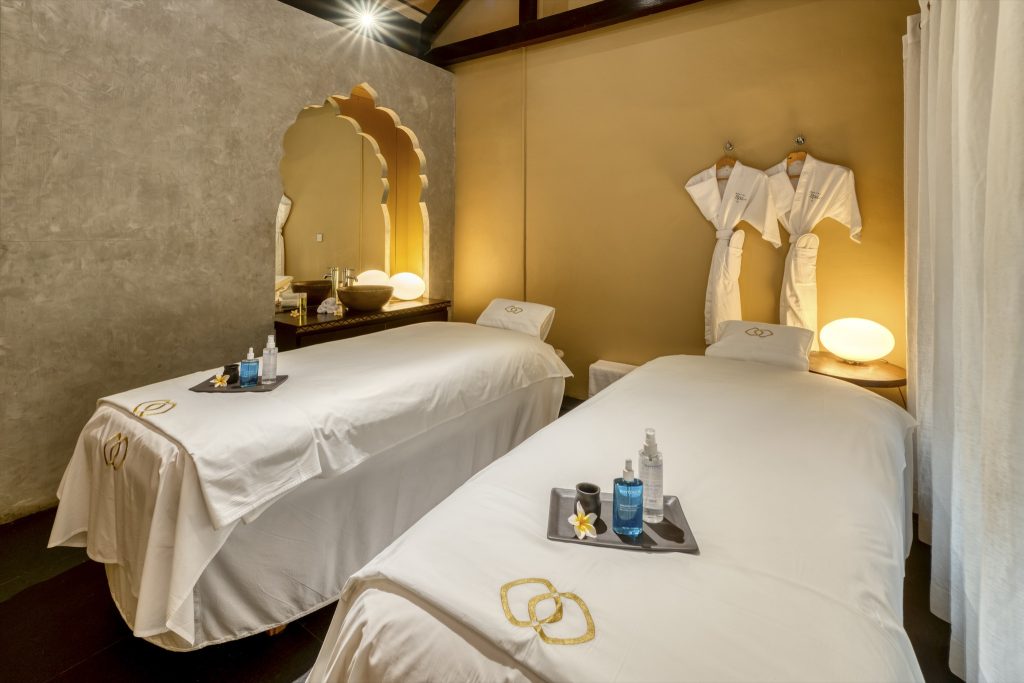 Behandlungsraum im Sofitel Mauritius L'Impérial Resort & Spa mit zwei Massageliegen, weißen Bademänteln und indirekter.
