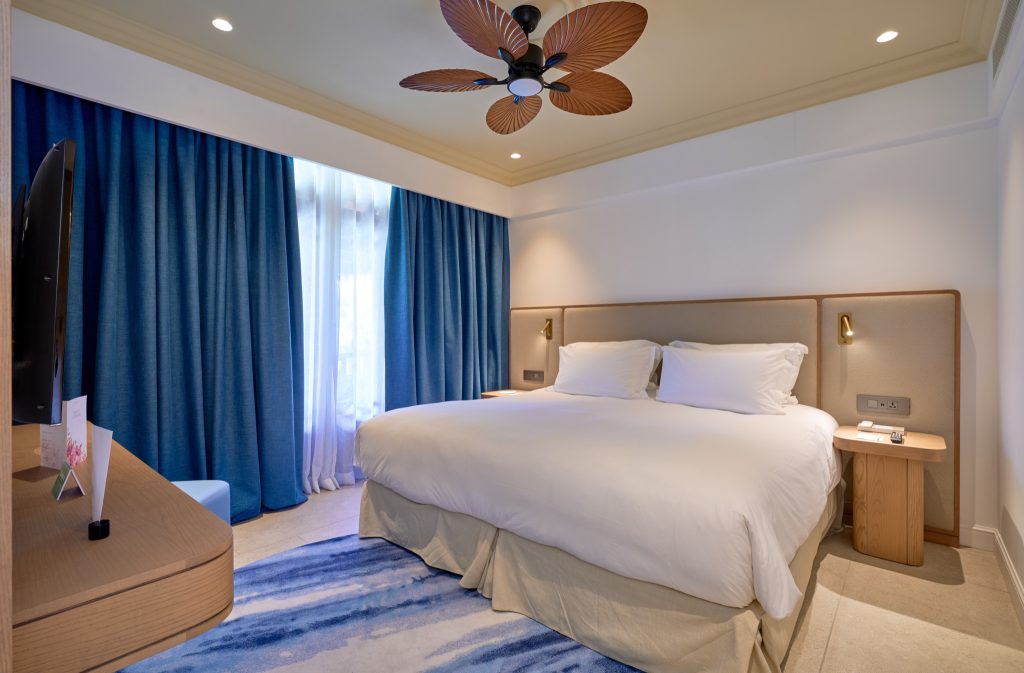 Modernes Family Suite Zimmer mit großem Doppelbett, Flachbildfernseher, blauen Vorhängen und Deckenventilator