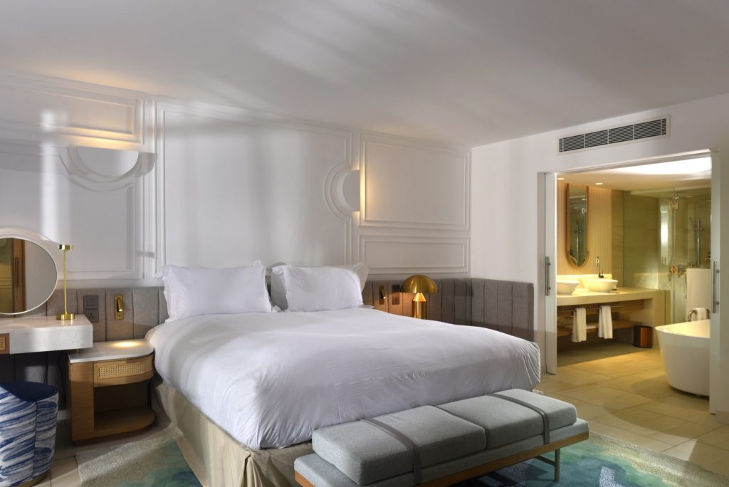 Modernes Hotelzimmer mit großem Doppelbett, weißer Bettwäsche, Holz-Kopfteil und offenem Bad