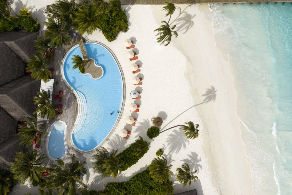 Luftaufnahme des Sun Siyam Iru Veli Poolbereichs mit nierenförmigem Pool, Holzdeck, Palmen und weißen Sonnenschirmen