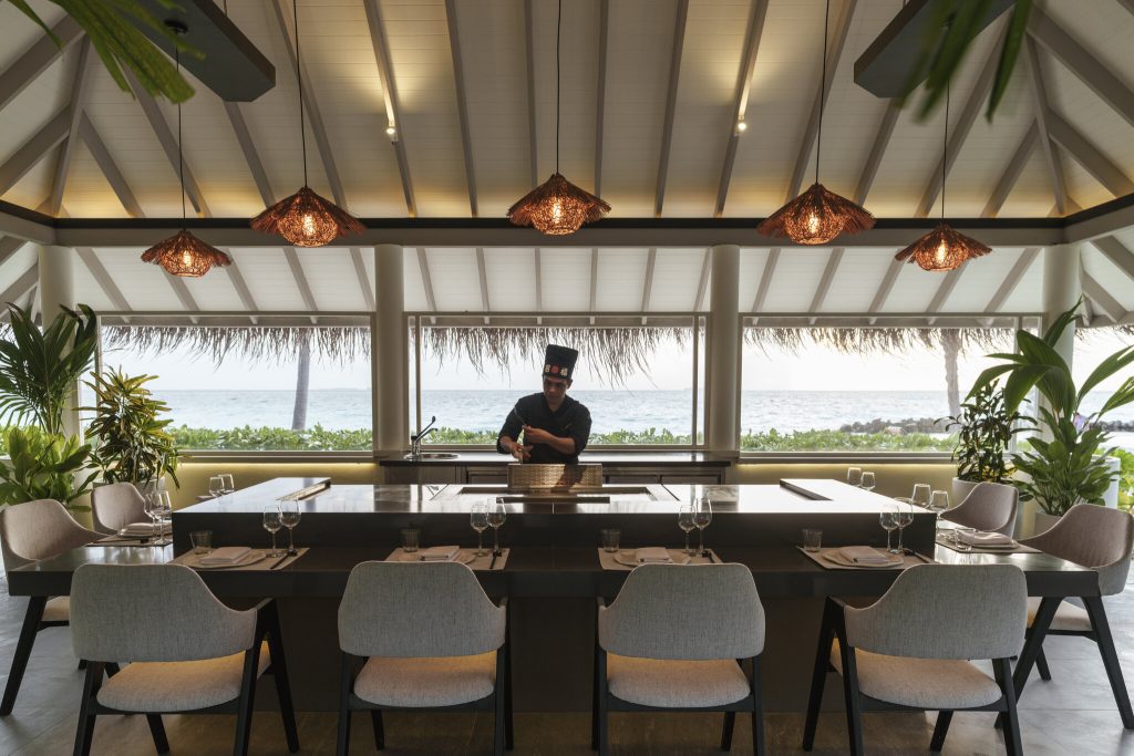 Küchentheke mit acht grauen gepolsterten Stühlen, gedeckten Tischsets und Koch in Sun Siyam Iru Veli restaurant-tappenyaki