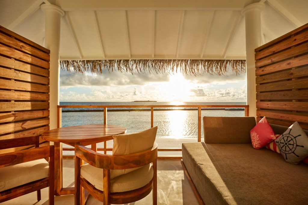 Terrasse der Beach Residence mit Holzmöbeln, bunten Kissen und direktem Blick auf das Meer bei Sonnenuntergang