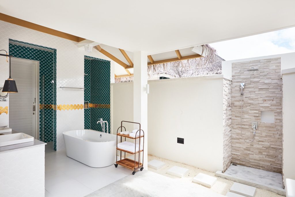 Modernes Badezimmer mit freistehender weißer Badewanne, türkis-goldenen Kacheln und Außenbereich mit Natursteindusche