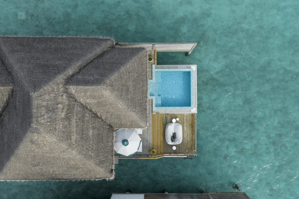Überwasservilla Sun Siyam Iru Veli Ocean Villa mit Holzdeck, Mosaikpool, Sonnenschirm und Gartenmöbeln über türkisfarbenem.