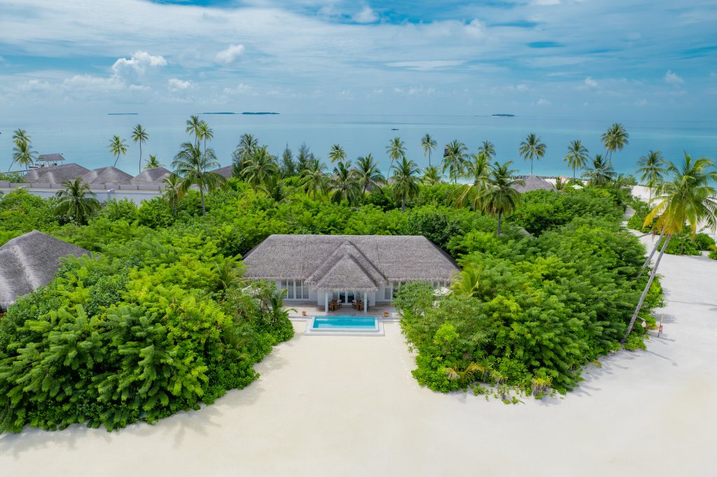 Ebenes Gebäude mit Strohdach, umgeben von Palmen und grünem Laub, mit rechteckigem Pool und Meer im Hintergrund