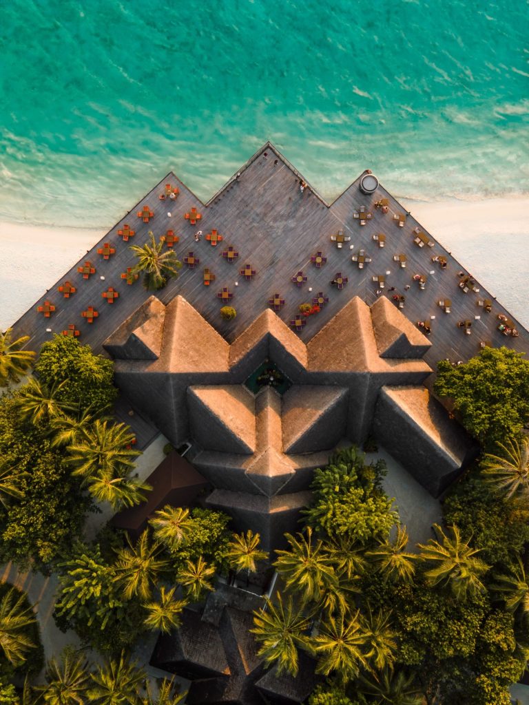 Vogelperspektive auf Sun Siyam Olhuveli Strandhotel mit geometrischen Dächern und Holzterrasse am türkisfarbenen Meer