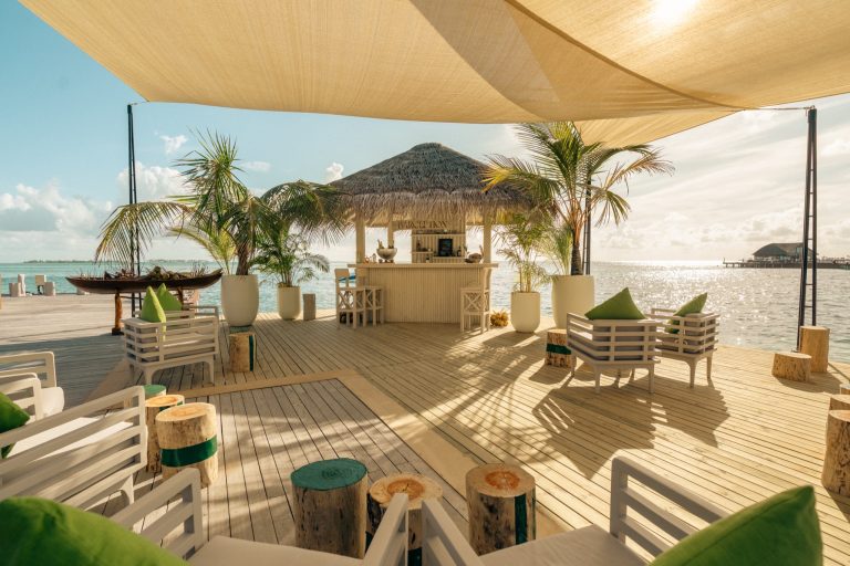 Bar Barception auf Sun Siyam Olhuveli mit Holzterrasse, Strohdach, Palmen in weißen Pflanzgefäßen und Meer im Hintergrund