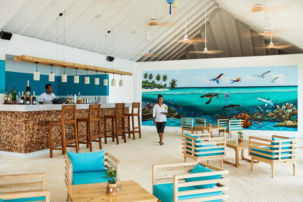 Offene Hotelbar mit Holzverkleidung, Mosaikmuster, hellen Stein-Theke und Bambuslampen im Sun Siyam Olhuveli Malediven