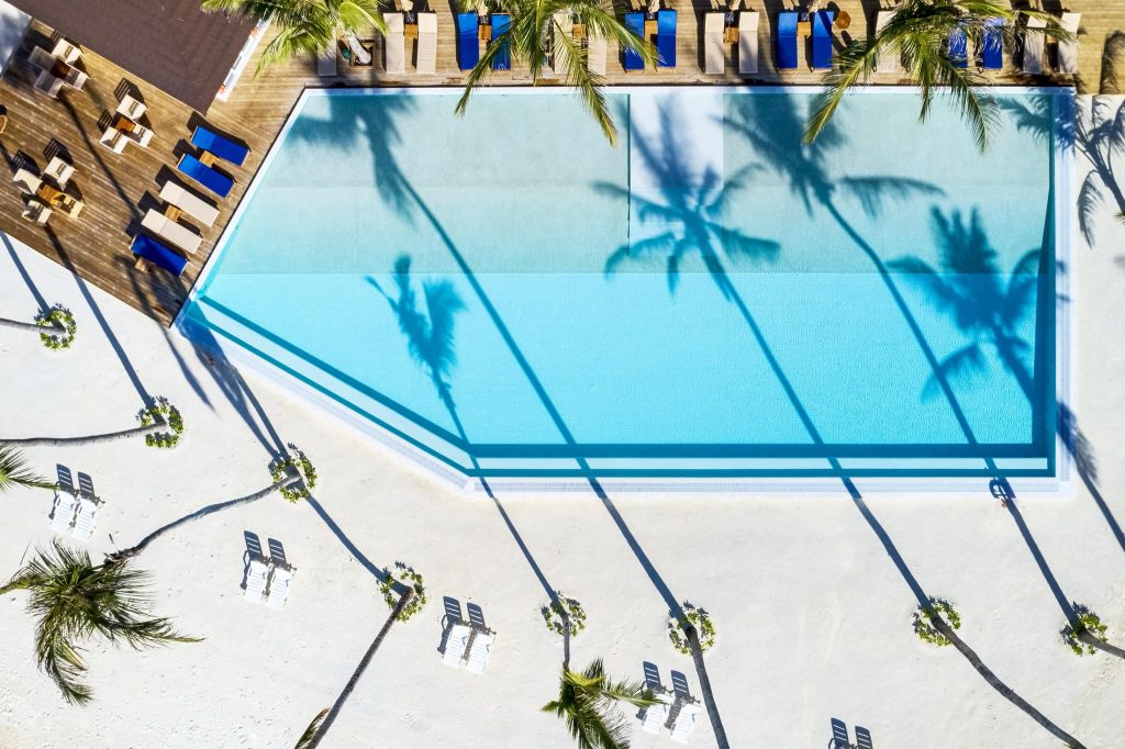 Draufsicht auf Sun Siyam Olhuveli Pool mit Holzterrasse, Liegestühlen, blauen und beigen Sonnenschirmen