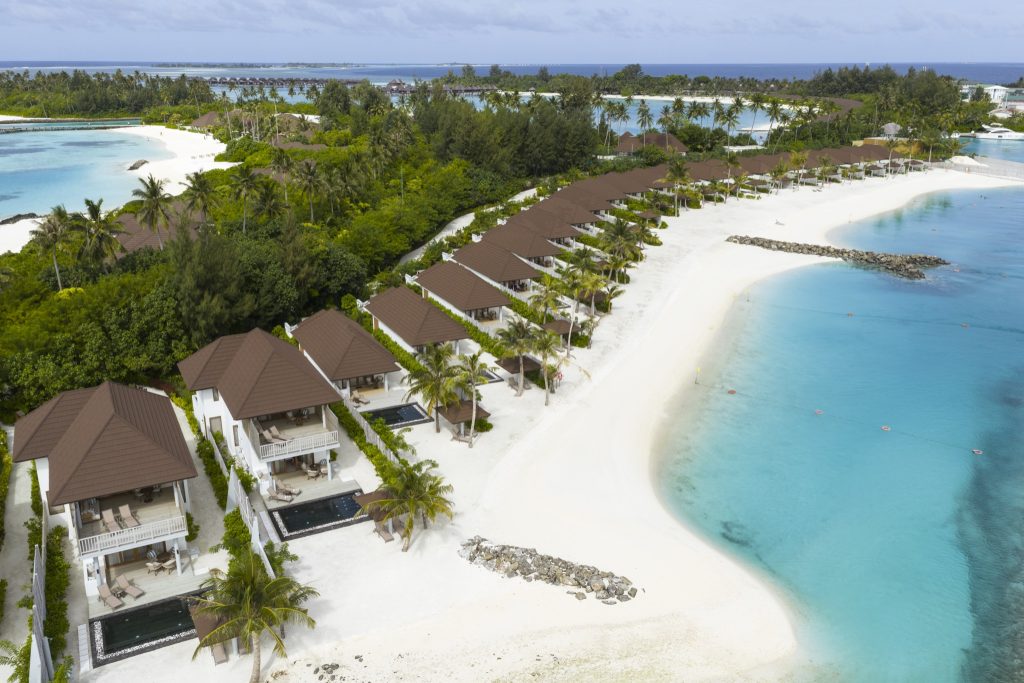 Luftaufnahme der Strandvillen mit braunen Dächern und privaten Pools am weißen Sandstrand