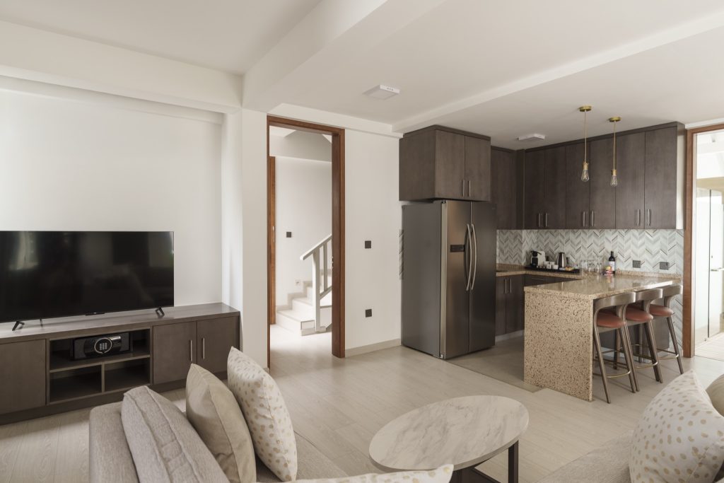 Moderner Hotelraum mit Küche und Wohnzimmer, dunkle Holzschränke, graues Sofa und Flachbildfernseher