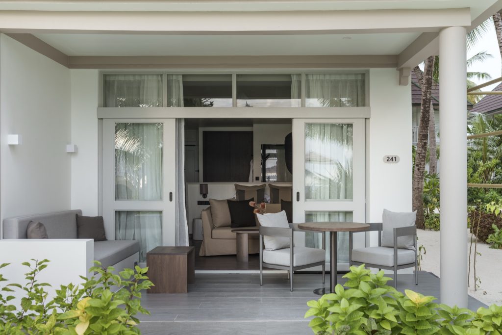 Terrasse eines Beach Pavilion Zimmers mit Holztisch, grauen Stühlen und Sofa auf den