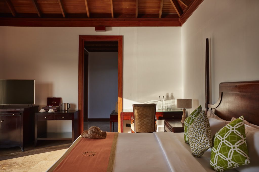 Zimmer der Deluxe Water Villa im Sun Siyam Olhuveli mit großem Bett, dunklen Holzmöbeln und freiliegenden Holzbalken
