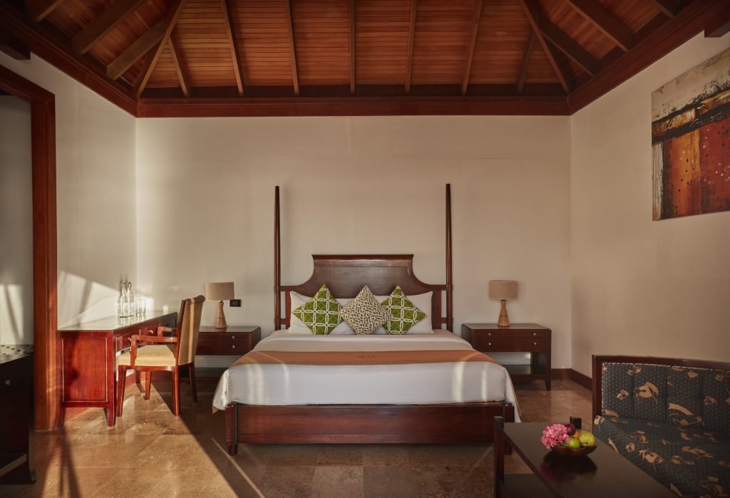 Deluxe Water Villa Zimmer mit hölzernem Himmelbett, Nachttischen, Tischlampen und hellbraunen Fliesen im Sun Siyam Olhuveli