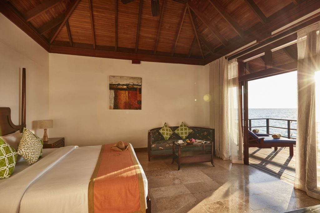 Deluxe Water Villa Zimmer im Sun Siyam Olhuveli mit Holzbalkendecke, großem Bett, Sitzgruppe und Balkon mit Meerblick