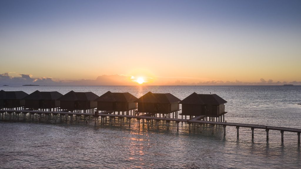 Überwasser-Bungalows aus Holz auf Stelzen, verbunden durch Holzstege bei Sonnenuntergang auf den
