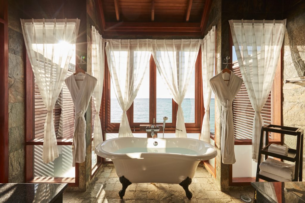 Freistehende Badewanne mit Löwenfüßen in deluxe water villa, große Fenster mit weißen Vorhängen, Meerblick auf den