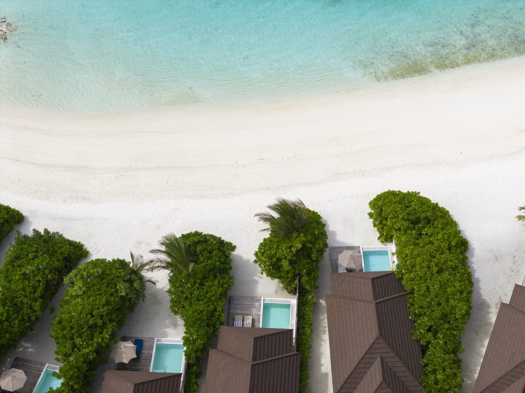 Vogelperspektive der Grand Beach Villa mit dunkelbraunen Ziegeldächern, privaten Pools und weißem Sandstrand