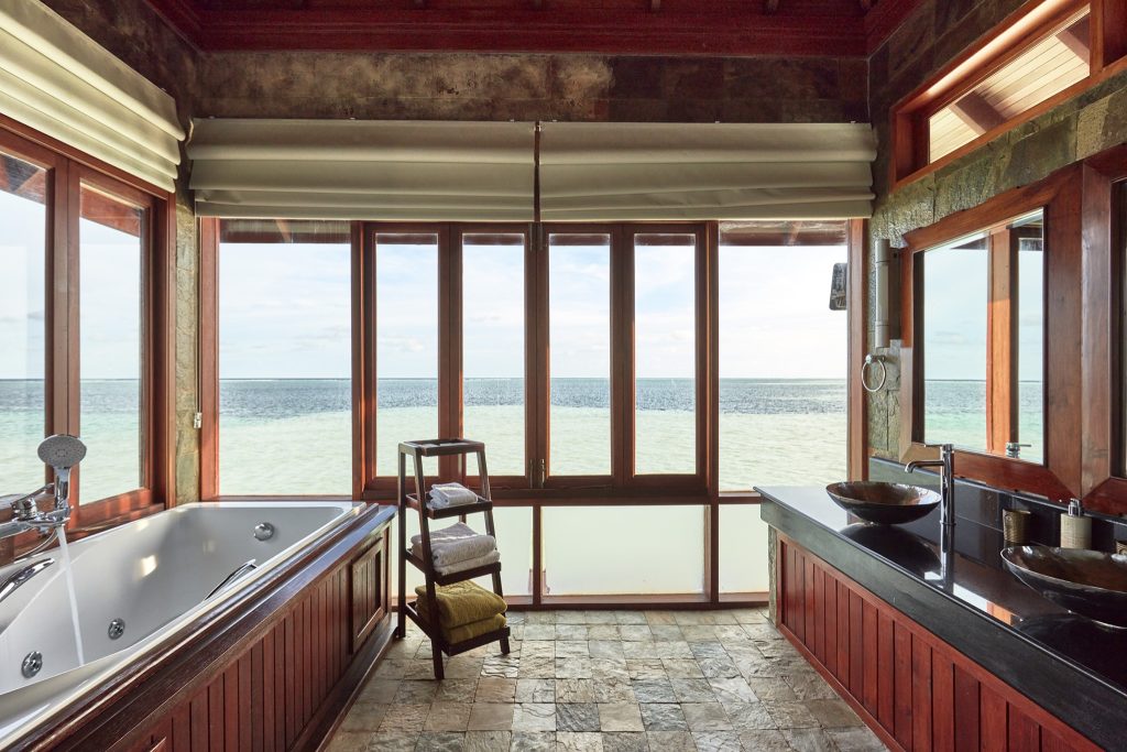 Badezimmer der Presidential Suite im Sun Siyam Olhuveli mit großer Badewanne, dunklem Holz und Fensterfront zum Meer