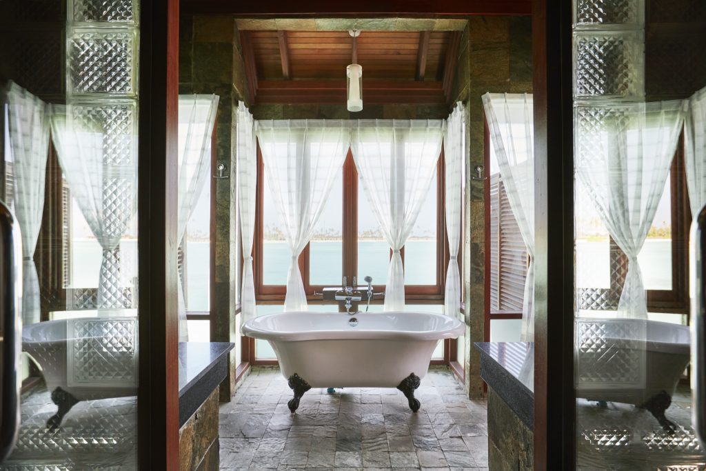Freistehende Badewanne in Prestige Jacuzzi Water Villa mit Natursteinwänden, Holzdecke und Blick auf Wasserlandschaft